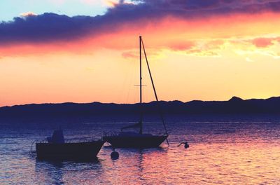 Sailboats moored on sea against sunset