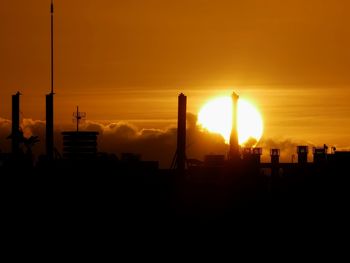 Silhouette built structures on field against sky during sunset