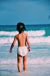 Rear view of shirtless man standing on beach against clear sky