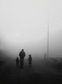 Rear view of silhouette father with children walking on footpath during foggy weather