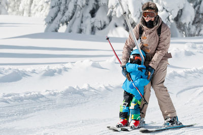 Portrait of mature woman teaching son skiing on snow covered field