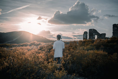 Rear view of man standing on mountain against sky during sunset