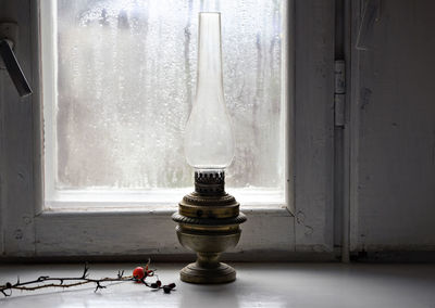 Soft focus on vintage oil lamp on the windowsill with twig in blurred rainy window background.