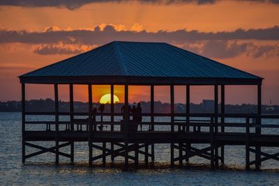 Silhouette deck chairs by sea against sky during sunset