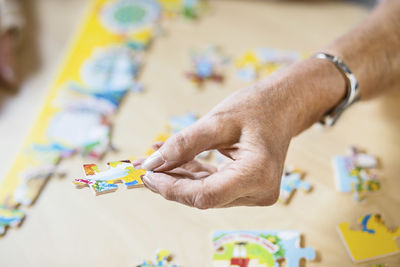 Cropped image of senior woman's hand holding jigsaw piece at table in nursing home