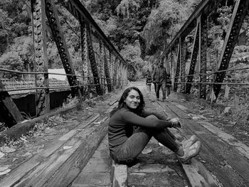 Monochrome portrait of a young woman sitting on a wooden footbridge