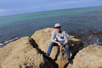 Man sitting on rock by sea against sky