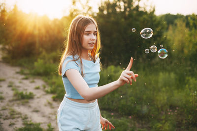 Cute girl with a beautiful smile catches soap bubbles on the background of a beautiful sunset