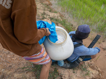 Low section of man holding container while standing by friend on rock