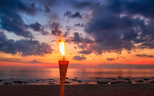 Scenic view of sea and a torch against sky during sunset