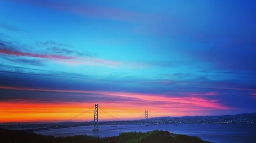 Suspension bridge over sea against sky during sunset