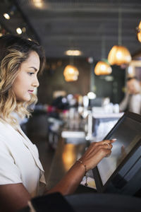 Side view of female owner touching cash register at checkout in restaurant