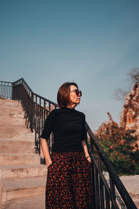 Woman standing by railing against sky