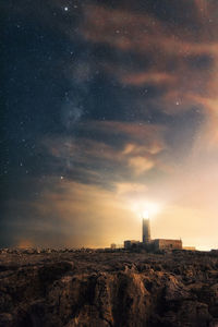 Lighthouse amidst buildings against sky at night