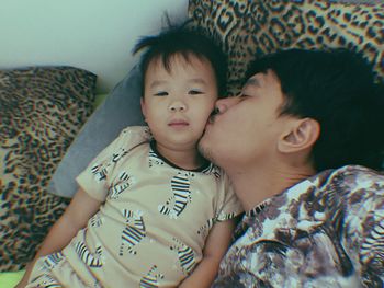 High angle view of father kissing boy while lying on bed at home