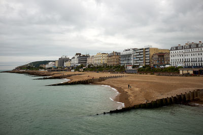 View of buildings by sea against cloudy sky