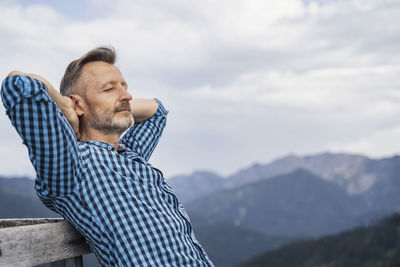 Man relaxing on mountain against sky