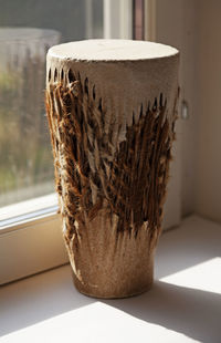 A tall traditional drum standing in the windowsill with sunlight