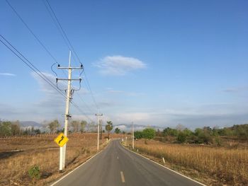 Road by electricity pylons against sky