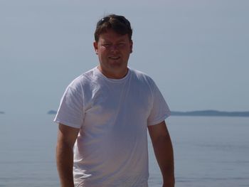 Portrait of mature man standing at beach against clear sky