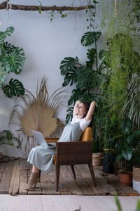 Beautiful businesswoman with hands behind head and computer relaxing, daydreaming in surround plants