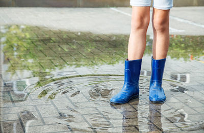 Low section of girl in rubber boots standing on puddle 
