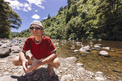 Man crouching by river against trees