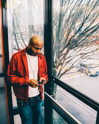 Full length of man using mobile phone while standing by window