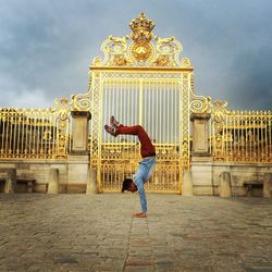 Full length of man practicing handstand against golden gate on footpath