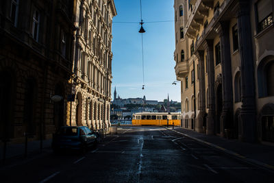 Street amidst buildings in city against sky and tram