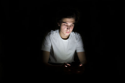 Young man with illuminated mobile phone sitting in darkroom