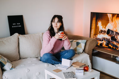 Young woman using mobile phone while sitting on sofa at home