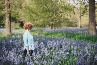 Woman standing amidst purple flowering plants at forest