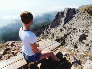 Woman sitting on cliff against sky