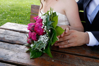 Midsection of bride and groom sitting by rose bouquet on table