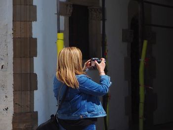 Woman photographing while standing against building