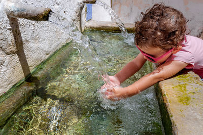 Cute girl cleaning hands in running water from faucet