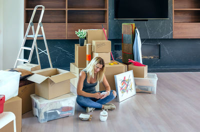 Full length of woman using mobile phone by cardboard boxes on floor