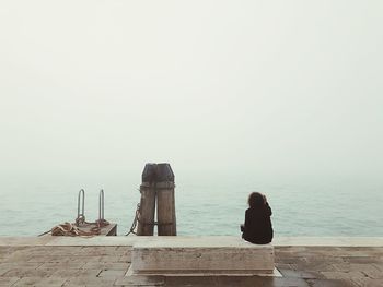 Rear view of man on wooden post by sea against sky