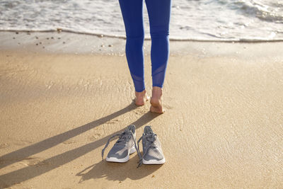 Woman walking barefoot on the beach, shoes in focus, shallow dof