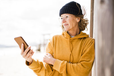 Smiling mature woman wearing eyeglasses using smart phone