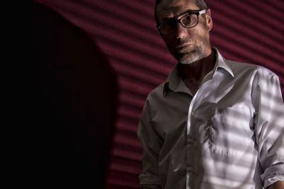 Low angle portrait of man wearing eyeglasses standing against wall