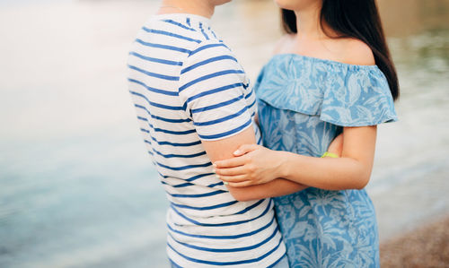 Midsection of couple standing against water