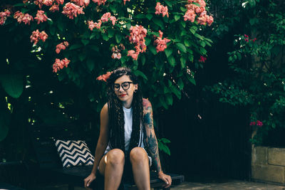 Young woman wearing sunglasses sitting on seat against plants