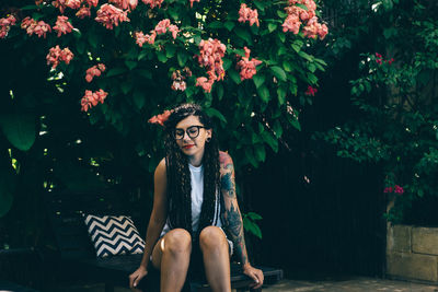 Young woman sitting on chair against flowering plants