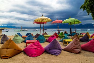 Bean bags and umbrellas at beach against cloudy sky