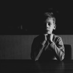 Portrait of serious boy with hands on chin sitting at home