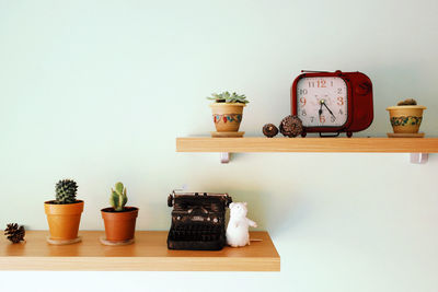 Old-fashioned typewriter and alarm clock with potted plants on shelves against wall