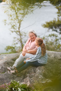 Grandmother and granddaughter talking while sitting on rock in park