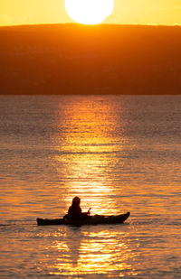 Silhouette person in sea against sky during sunset